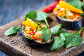 Baked stuffed eggplant with peppers, cheese and tomatoes on rustic wooden table, vegetarian food.