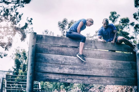 Fit man and woman climbing on wooden wall during obstacle course