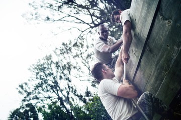 Soldiers helping man to climb wooden wall