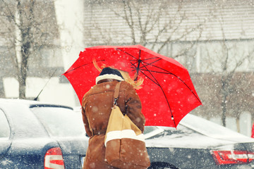 Woman with red umbrella walking on heavy snow
