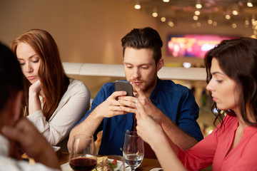 leisure, technology, lifestyle and people concept - friends with smartphones dining at restaurant