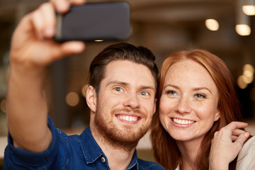 leisure, technology and people concept - happy couple taking selfie by smartphone at restaurant