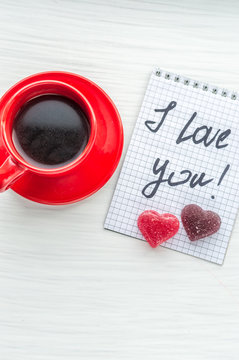 Cup of coffee, a candy in the shape of a heart and a note I love you. Vertical photo