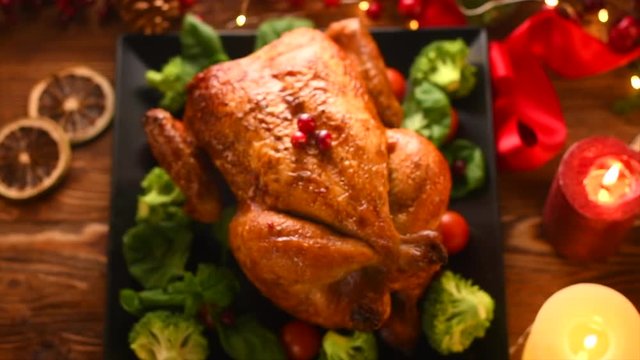 Christmas dinner. Roasted chicken on holiday table, decorated with candles. Delicious steamed roast chicken over wooden background. Top view, flatlay. 4K UHD video footage. Slow motion 3840X2160