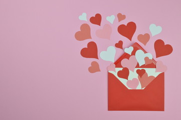 white blank letter in open red envelope with lots of different red, pink and white paper hearts coming out and spread over the pink background as love letter with copy space to the left