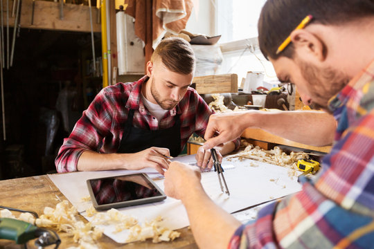 profession, technology and people concept - two carpenters with dividers or compass and ruler measuring blueprint at workshop