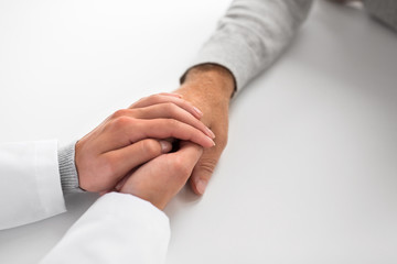 Fototapeta premium medicine, healthcare and old age concept - close up of young doctor holding senior patient hand