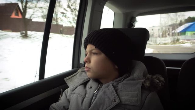Young Boy Sitting on the back seat in a car listening to music and looking around in a different mood, winter weather, healthy lifestyle. Travel