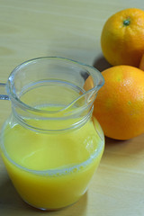 Orange juice in jug and orange fruits on table. Vertical image with copy space.