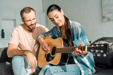 handsome husband teaching beautiful wife to play acoustic guitar