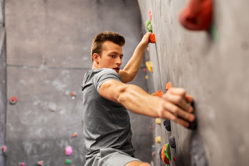 fitness, extreme sport, bouldering, people and healthy lifestyle concept - young man exercising at indoor climbing gym - obrazy, fototapety, plakaty