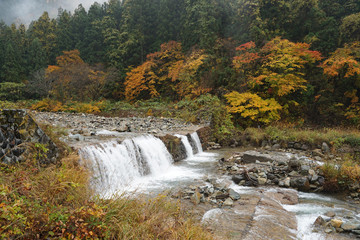 Beautiful autumn landscape of waterfall with large rocks and mountain background