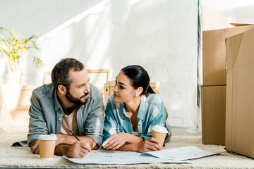 husband and attractive wife lying on floor, drinking coffee and working on blueprints of new house at home, moving concept