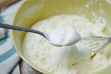 Adding spoon of sour cream to the dough. Process of mixing eggs, preparing pie. Top view with light colors. Kitchen Objects.