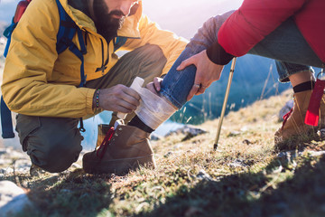 A woman has sprained her ankle while hiking, her friend uses the first aid kit to tend to the injury - Powered by Adobe