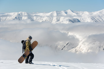 Naklejka na ściany i meble Man walking with the brown snowboard in the mountain resort