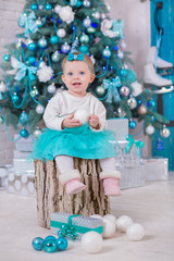Cute baby girl posing close to christmas tree and blue wooden door in cozy home studio.