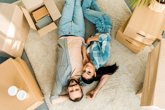 top view of smiling couple lying on floor and relaxing after packing for new house, moving concept