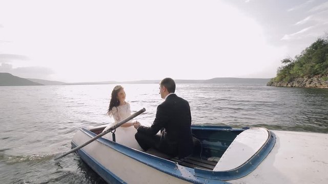 Young and beautiful wedding couple together sailing on a boat with oars on the sea near the mountains. Lovely groom and bride. Slow motion