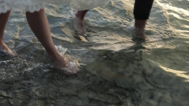 Young and beautiful wedding couple walking together on the beach. The legs of the bride and groom go along the sea water. Slow motion
