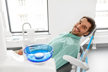 medicine, dentistry and healthcare concept - happy smiling male patient on chair at dental clinic