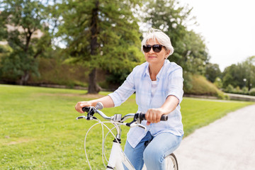 active old age, people and lifestyle concept - happy senior woman riding fixie bicycle at summer...