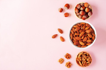Obraz na płótnie Canvas Assortment of nuts in bowls. Almond, hazelnut, walnut on pink background. Food mix background, top view, flat lay, copy space, minimal layout