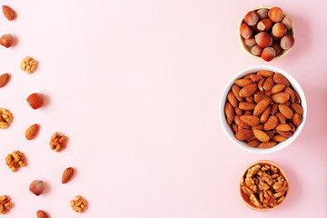 Assortment of nuts in bowls. Almond, hazelnut, walnut on pink background. Food mix background, top view, flat lay, copy space, minimal layout