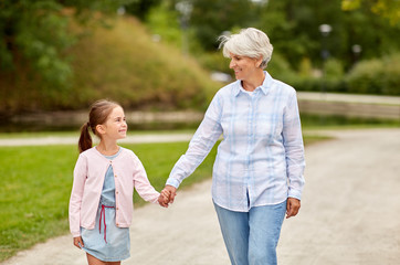 family, leisure and people concept - happy grandmother and granddaughter walking at summer park