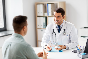 medicine, healthcare and diabetes concept - smiling doctor with glucometer and insulin pen device talking to male patient at medical office in hospital - Powered by Adobe