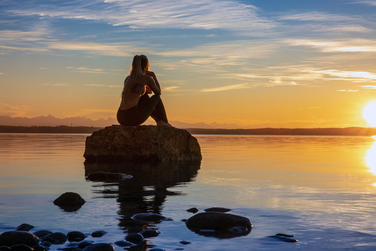 h&uuml;bsche junge frau macht yoga auf einem Stein im Wasser See Meer im Sonnenuntergang Abendrot