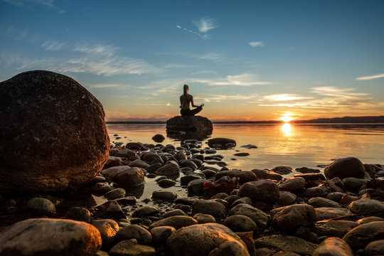 hübsche junge frau macht yoga auf einem Stein im Wasser See Meer im Sonnenuntergang Abendrot