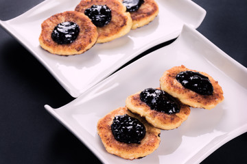 2 white stylish plates with cottage chesse pancakes and jam. Dessert on dark background.