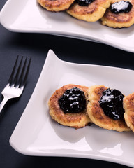 2 white stylish plates with cottage chesse pancakes and jam. Dessert on dark background, vertical image.