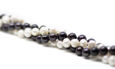 Two strands of white and black pearls intertwined on white background isolated