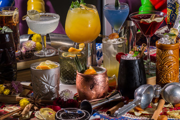 Whiskey-cola cocktail, mojito-cocktail, orange cocktail, strawberry cocktail in glass glasses with straws. Bar accessories: shaker, spoon, spices on a wooden stand