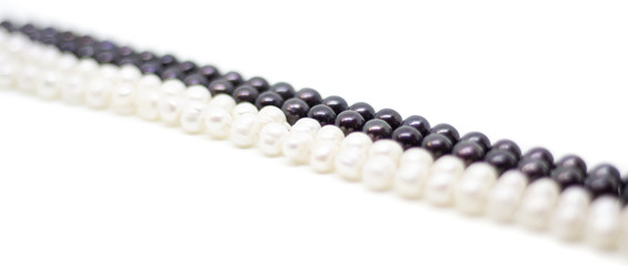 Two strands of white and black pearls intertwined on white background isolated