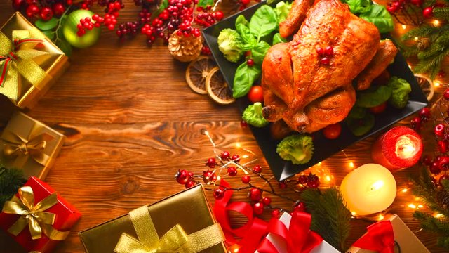 Christmas dinner. Roasted chicken on holiday table, decorated with gift boxes, burning candles and garlands. Roasted turkey over wooden background. Top view, flatlay. 4K UHD video footage 3840X2160