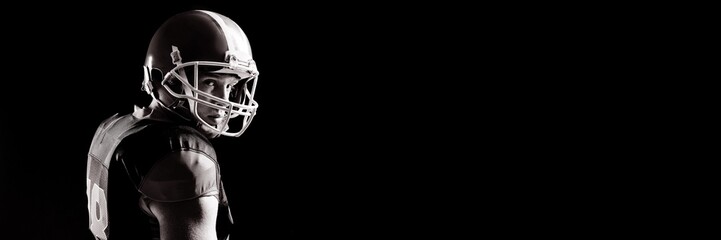 American football player in helmet standing against black