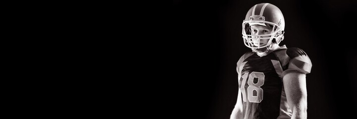 American football player in helmet standing against black