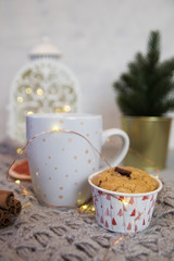 Winter still life from scarf, white mug of cocoa, coffee or hot chocolate, muffin, christmas tree on warm plaid with garland.