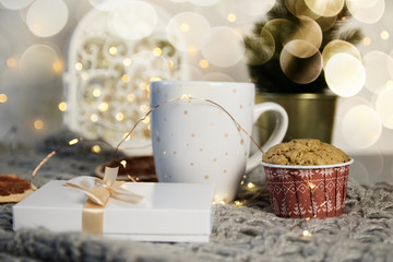 Winter still life from scarf, white mug of cocoa, coffee or hot chocolate, muffin, christmas tree on warm plaid with garland.