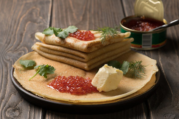 Traditional russian dish - thin pancakes with red caviar and open tin can with caviar on the background