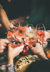 Traditional Christmas or New Year holiday celebration party. Friends or family feasting and clinking glasses with rose wine at festive Christmas table with homemade snacks