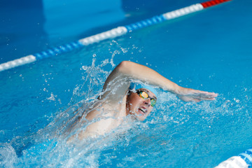 Image of athlete man in blue cap swimming in style of crawl in swimming pool