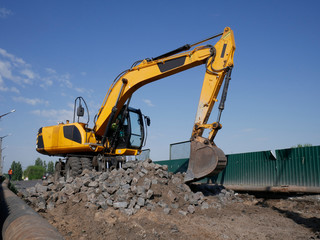 The yellow excavator works on repairing the road, stones, working on the road
