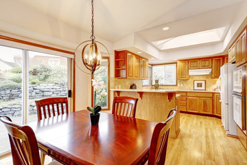 Kitchen interior with cherry wood dining room table and orange tone cabinets in large room.