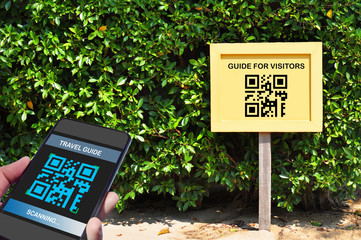 Hand holding smartphone with scanning QR code travel guide screen with guide for visitors sign,...
