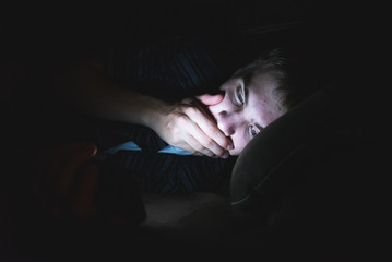 Teenager reading shocking news on his cell phone as he is lying on a couch in the dark.