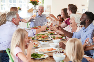 Group Of Multi-Generation Family And Friends Sitting Around Table And Making A Toast